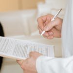 A medical professional in a white coat examines a clipboard with patient documents.